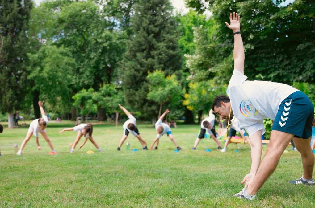 Kids stretching exercises in a park guided by a coach, promoting fitness and fun.