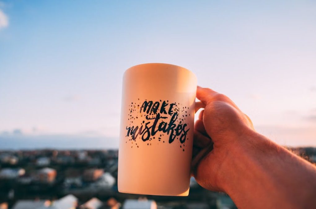 A hand holding a motivational mug with 'Make Mistakes' against a sunset in Lviv.