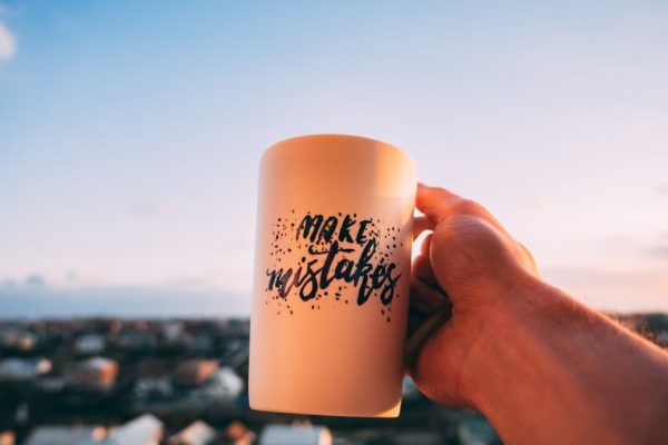 A hand holding a motivational mug with 'Make Mistakes' against a sunset in Lviv.